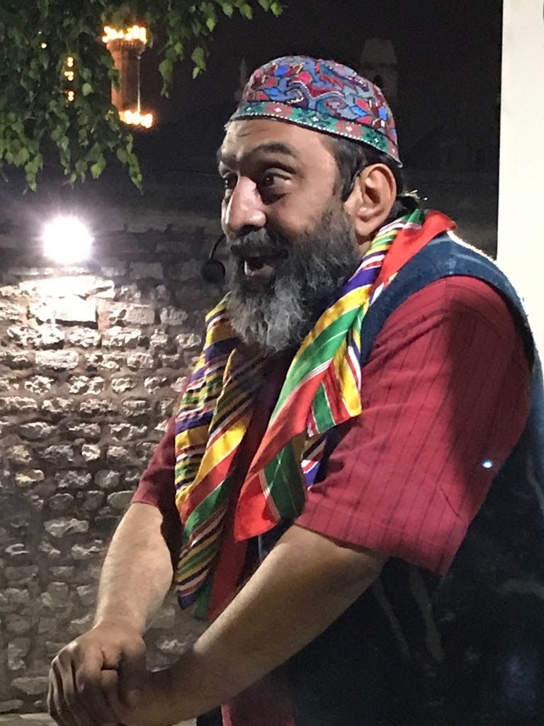 Meddah kıyafetiyle, taş duvar önünde